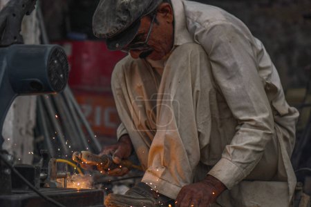 Poor old skilled Pakistani Welder welding pipes and metal rods in his street workshop