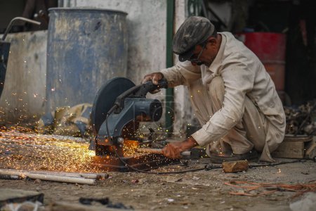 Poor old Pakistani Welder cutting pipes and metal rods in his street workshop with electric cutter causing flames and sparks