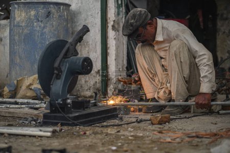 Pobre viejo y experto soldador paquistaní tubos de soldadura y varillas de metal en su taller de la calle
