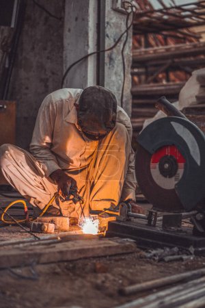 Welder welding pipes and metal rods with flaming sparks in his street workshop