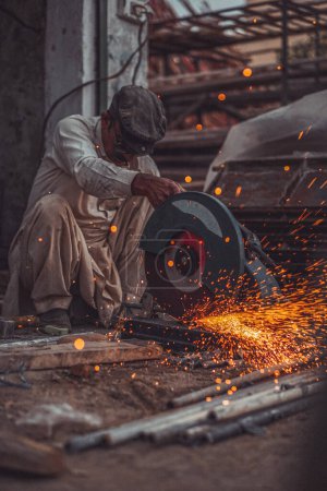 Photo for Welder cutting pipes and metal rods in his street workshop with electric cutter causing flames and sparks - Royalty Free Image