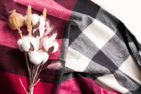 Photo for Bouquet of cotton, fluffy ears of lagurus, poppy. the bouquet lies on a marsala-colored checkered fabric. cozy background. - Royalty Free Image