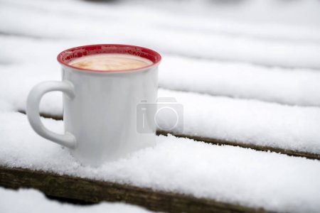 A cup of hot drink on a snowy wooden pallet. winter.