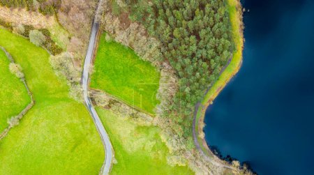 Aerial view of winding road beside Swinsty Reservoir in North Yorkshire, UK. Yorkshire Water reservoir bordered by coniferous woodland in countryside.