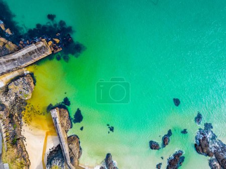 Aerial view of Port of Ness harbour with turquoise water in the Isle of Lewis in the Outer Hebrides. A sunny tranquil seascape scene with no people