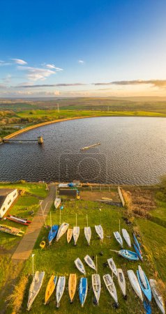 Aerial view of Reva Reservoir, West Yorkshire, with sailing boats and kayaks on the shore. Sunset lakeside image at golden hour. 