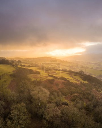 Sonnenaufgang über den Hügeln von Denbighshire, Wales, als die Sonne durch dunkle Wolken bricht und leichter Regen auf die Landschaft fällt