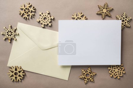 Photo for Christmas winter festive ornament. Blank paper card with wooden snowflake on brown background. Minimal decoration. Invitation Christmas holiday party. Flat lay, top view, copy space. - Royalty Free Image