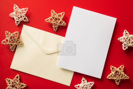 Photo for Christmas winter festive ornament. Blank paper card and envelope with wooden decoration on red background. Minimal decoration. Invitation Christmas holiday party. Flat lay, top view, copy space. - Royalty Free Image