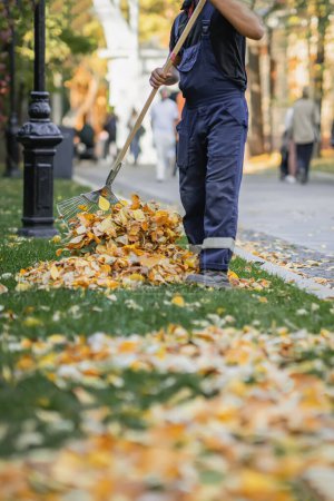 Foto de Hombre trabajador rastrillando hojas secas, limpiando hojas caídas en el parque de la ciudad. Otoño, concepto de caída de hojas - Imagen libre de derechos