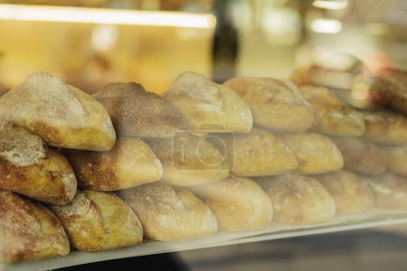 Photo for Stack of bread loaves are displayed in a window. The bread is white and he is freshly baked. Blurred view through store window - Royalty Free Image