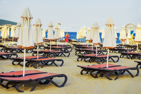 Playa vacía de arena forrada con sombrillas blancas y sillones rojos. Serenidad junto a la playa
