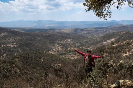 Foto de Un hombre está de pie en una colina con los brazos extendidos en el aire, con una vista de las montañas en la distancia. - Imagen libre de derechos