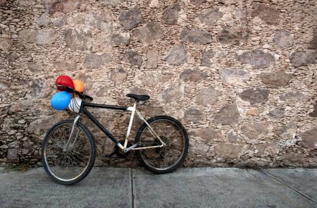 Foto de Una vieja bicicleta con globos de colores descansando sobre una vieja pared de roca en México, con espacio para texto - Imagen libre de derechos