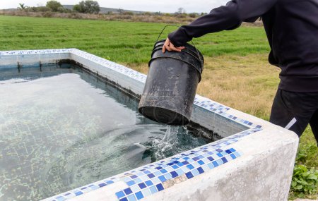 Eine Person, die Wasser aus einem Becken schöpft, um den Garten zu bewässern, mit Platz für Text