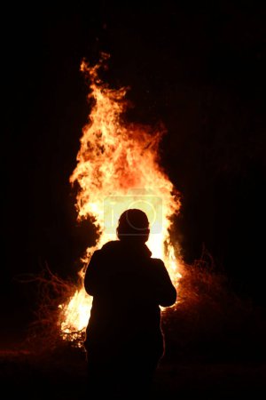 Une silhouette d'une personne qui regarde un grand feu dans le noir
