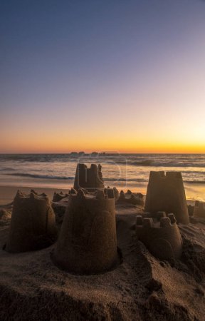 Téléchargez les photos : Un château de sable fait par des enfants sur la plage avec un beau coucher de soleil sur la plage, avec espace pour le texte - en image libre de droit