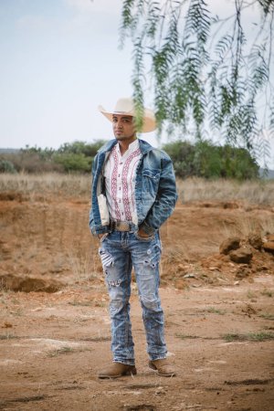 A cowboy wearing jeans and a hat, standing under the sky with fluffy clouds, working on a farm