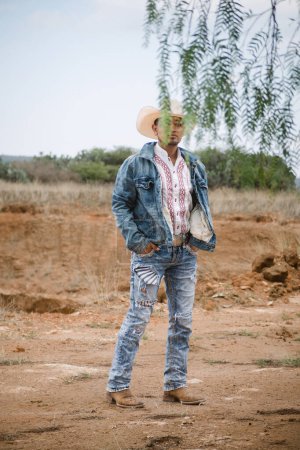 Photo for A cowboy wearing jeans and a hat, standing under the sky with fluffy clouds, working on a farm - Royalty Free Image