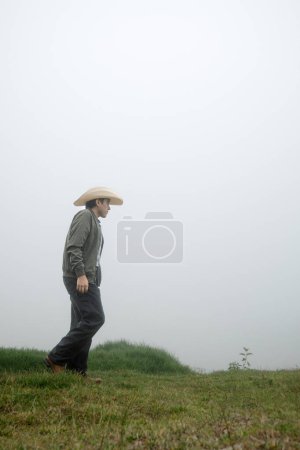 A man with cowboy boots strolls amidst the fog covered grasslands of Mexican Hat, embracing the serene beauty of nature.