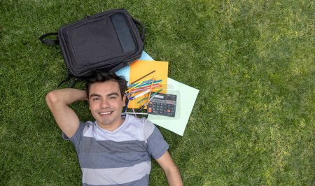 Junger Student liegt mit Rucksack und Schulsachen im Gras