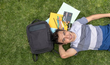 Junger Student liegt mit Rucksack und Schulsachen im Gras