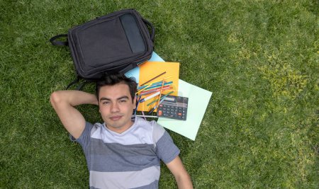 Male student lying on the grass with a backpack and a calculator