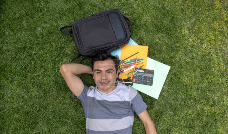 Male student lying on the grass with a backpack and school supplies