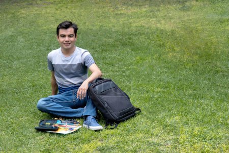 Jeune étudiant assis sur l'herbe avec un sac à dos et des fournitures scolaires