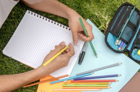 Student person writing in a notebook with colored pencils