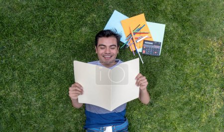 Männlicher Student liegt im Gras und liest ein Dokument