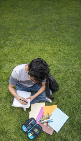 Photo for Student sitting on the grass writing in a notebook - Royalty Free Image