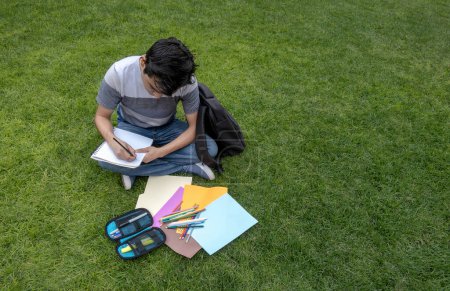 Student sitting on the grass writing in a notebook