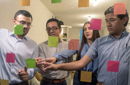Ein buntes Team junger Leute im Amt betrachtet klebrige Zettel auf Glas-Brainstorming