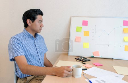 man sitting at a desk with a whiteboard and a cup of coffee
