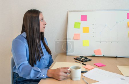 woman sitting at a desk with a whiteboard and a cup of coffee