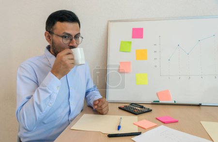 man sitting at a desk drinking from a white mug