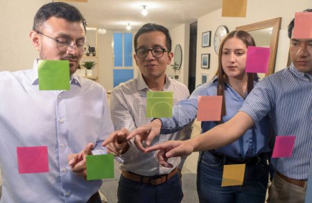 A Group Of People Standing Around A Glass Wall With Sticky Notes On Them