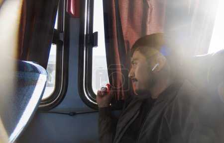 Un joven sonriente viajando y sentado en un autobús económico, con espacio para el texto