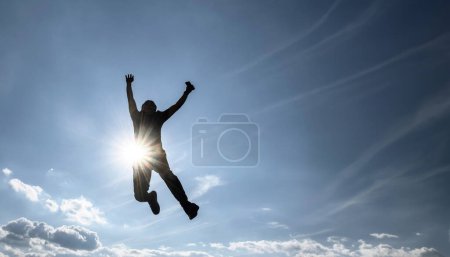 Téléchargez les photos : Un homme sautant avec un fond de ciel plein, les rayons du soleil, profitant d'un moment de succès, avec de l'espace pour le texte - en image libre de droit