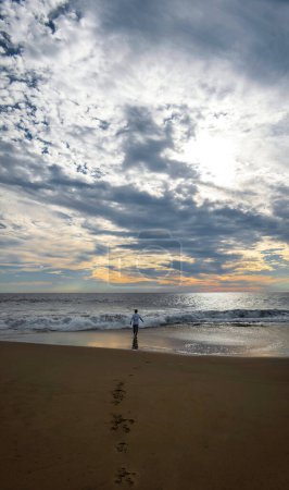 Ein junger Mann am Strand blickt auf den Sonnenuntergang, reflektiert, Raum für Text