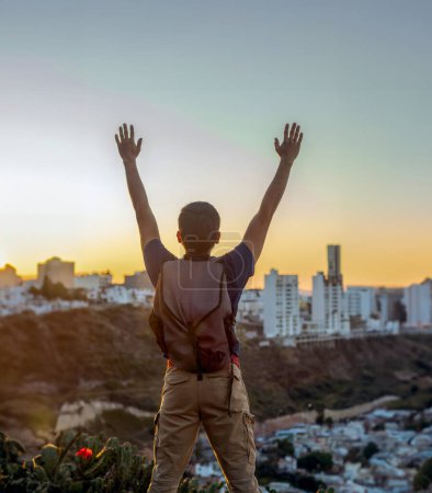 Téléchargez les photos : Un jeune homme puissant levant les mains vers le ciel sur un coucher de soleil haut au-dessus de la ville - en image libre de droit