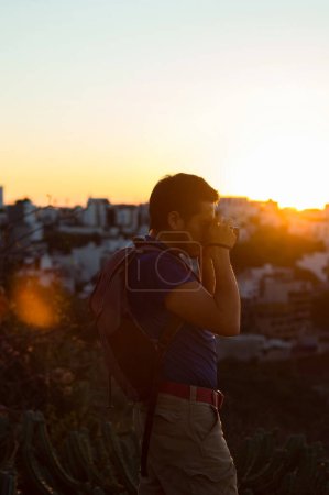 Un joven tomando una foto con su cámara al atardecer, con espacio para el texto