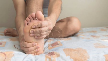Ein Mann massiert seinen Fuß gegen Schmerzen in Sohle, Ferse, Fußgewölbe und Zehen. Platz für Text rechts.