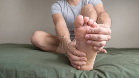 Eine Person massiert ihren Fuß wegen Schmerzen in der Sohle, im Fußgewölbe und in den Zehen. Platz für Text links.