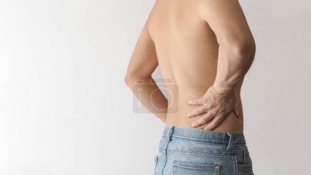 Un hombre sin camisa girando la espalda y tocando la parte baja de la espalda con la mano debido al dolor, fondo blanco con espacio para el texto a la izquierda