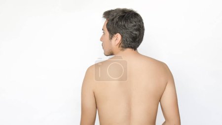 Eine Rückansicht eines jungen erwachsenen Mannes ohne Hemd, der nach links schaut, mit Platz für Text auf der linken Seite, vor weißem Hintergrund.