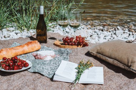 Photo for Summer romantic rustic picnic on the coast with white wine glasses, bottle, baguette, cherries, cheese, grape, open book. Sea beach. Vacation and rest. - Royalty Free Image