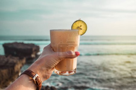 Photo for Hand with glass of cocktail on the background of the ocean. Sunset on the sea. Healthy white drink. Bali, Indonesia, Canggu, Echo beach. Vacation time - Royalty Free Image