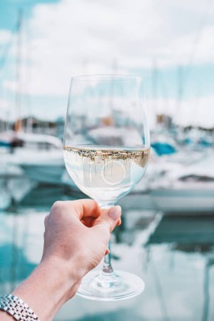 Photo for Woman hand with white wine, champagne glass on a yachts, sailing boats, building background. Vacation in Europe. Nice, French riviera, bay. Drink photo. Romantic relax, holiday on the sea coast. - Royalty Free Image